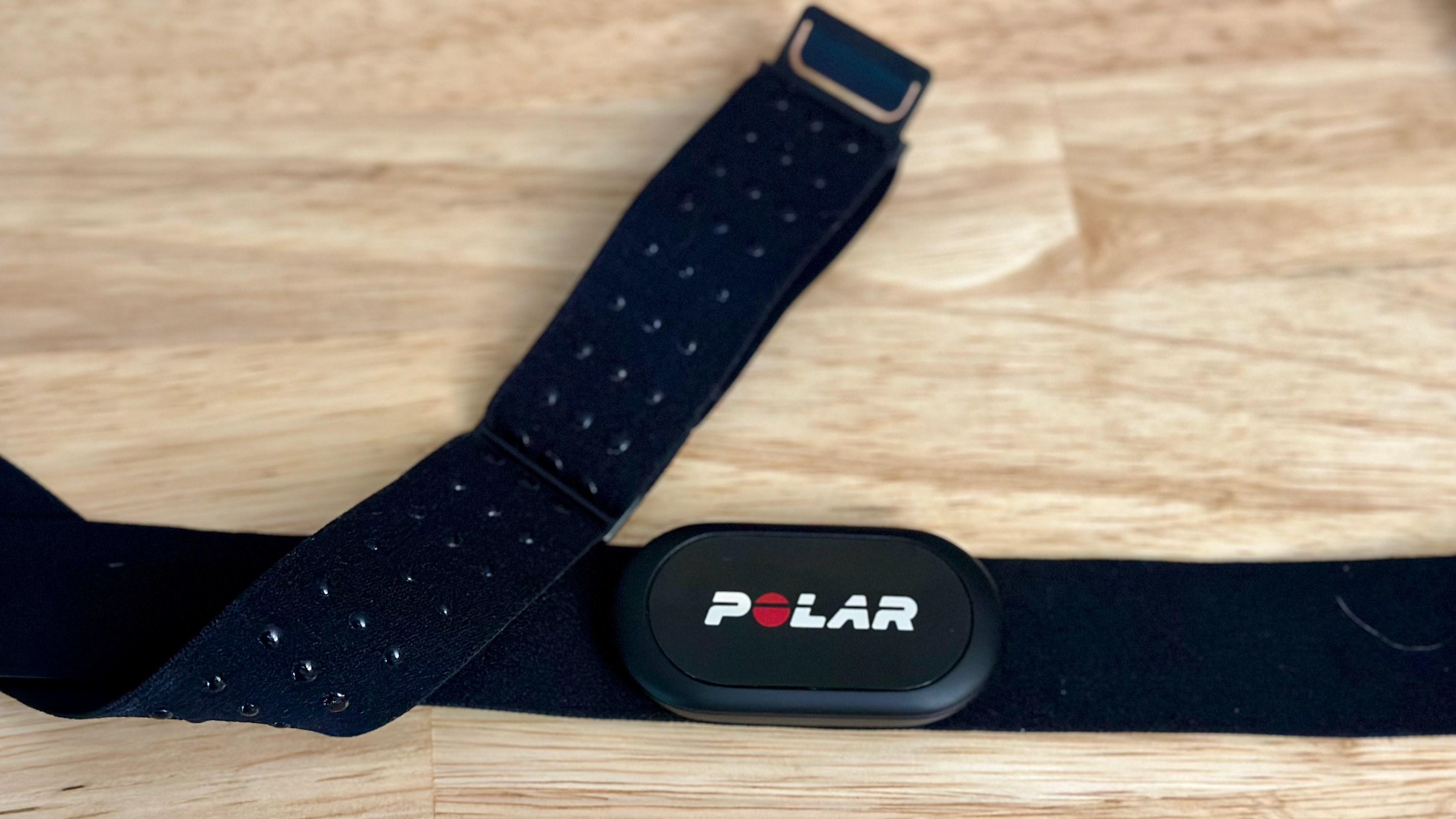 The Polar H10 and its electrode-covered strap sitting on a desk.