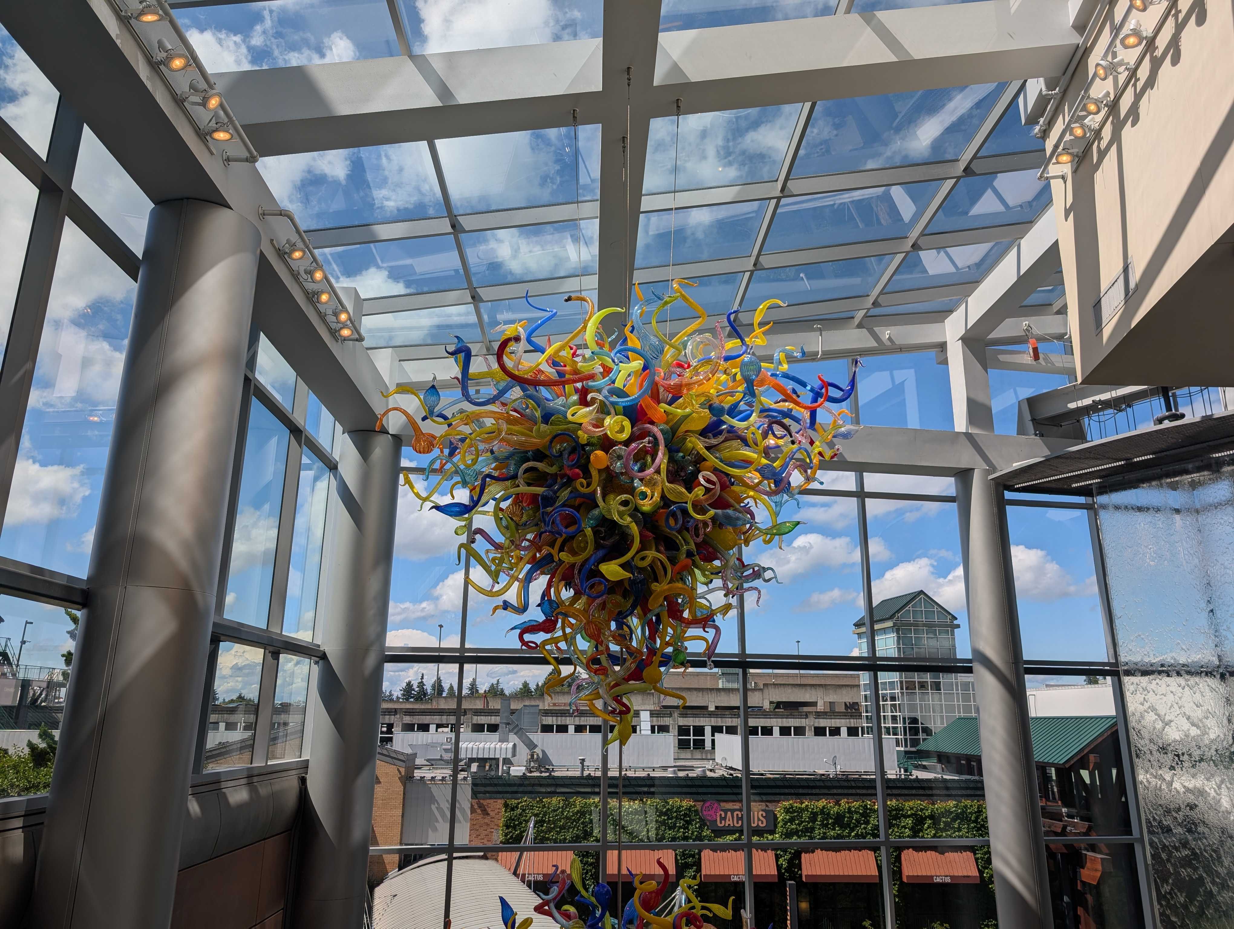 A piece of colorful glass art hanging from a glass ceiling