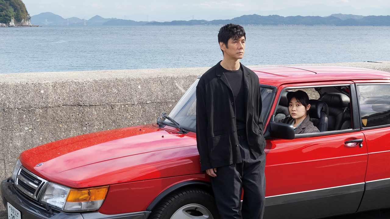 A man stands on the left side of a car as another person occupies the driver's seat in Drive My Car