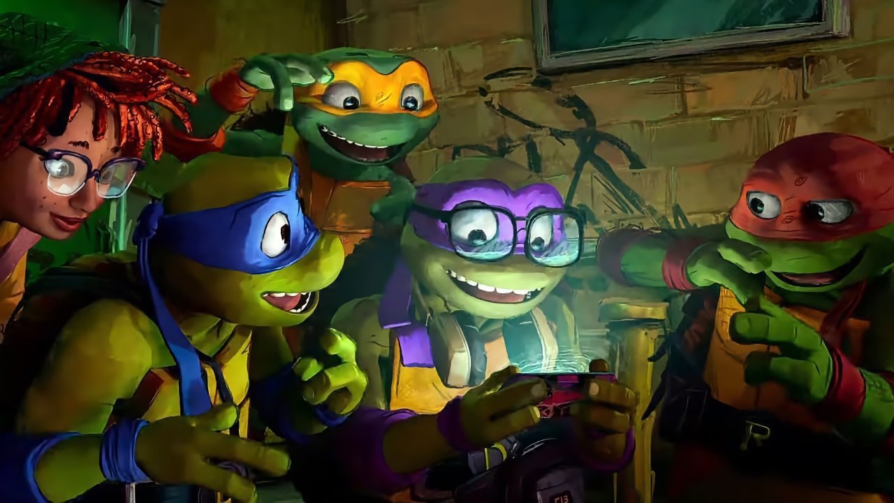 A group shot of the main heroes and April O'Neal looking at a phone in Teenage Mutant Ninja Turtles: Mutant Mayhem