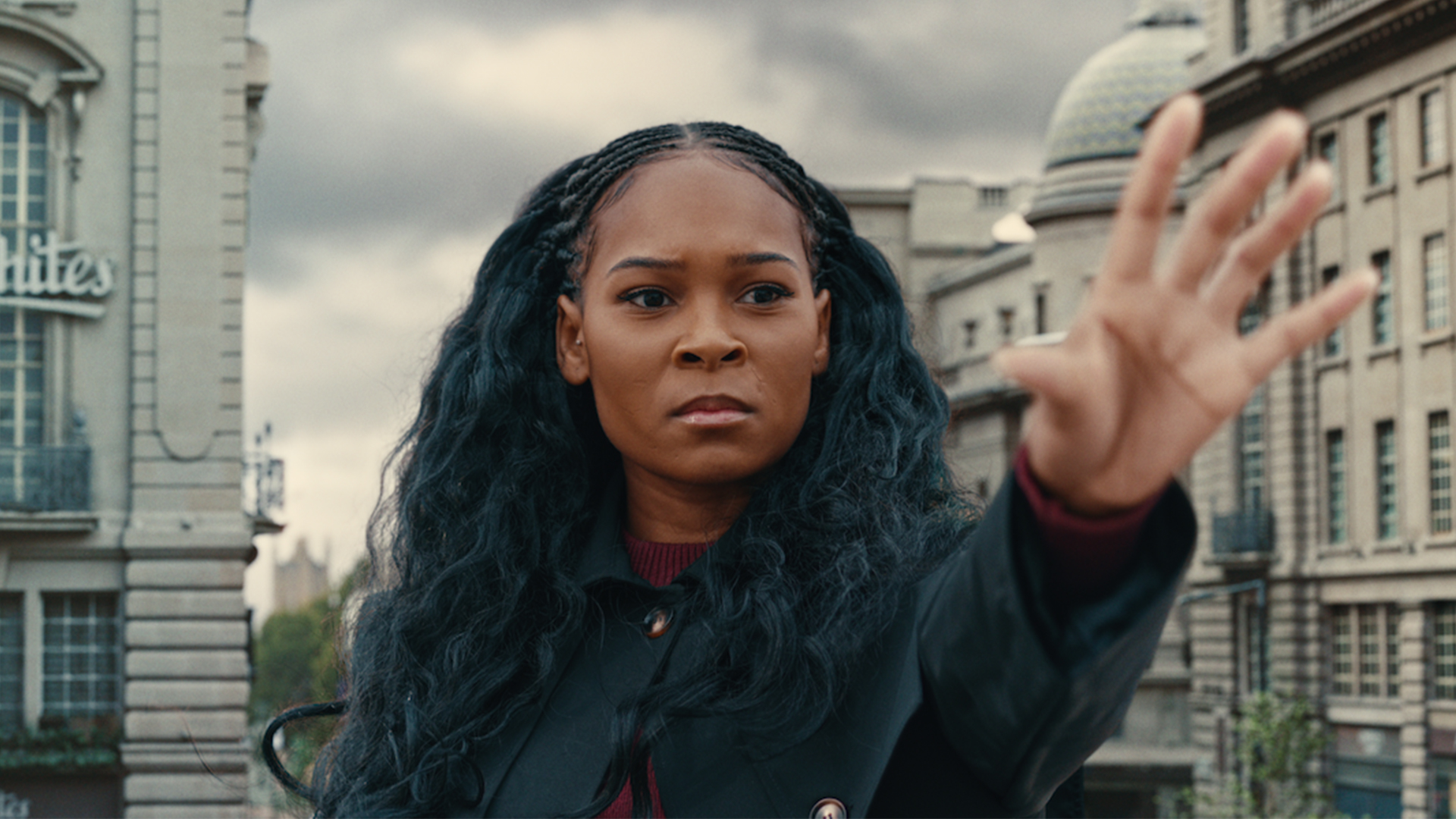 A women holds her hand up with buildings blurred in the background