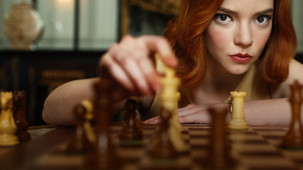 Beth Harmon with a concentrated look on her face as she moves a chess piece towards the camera.