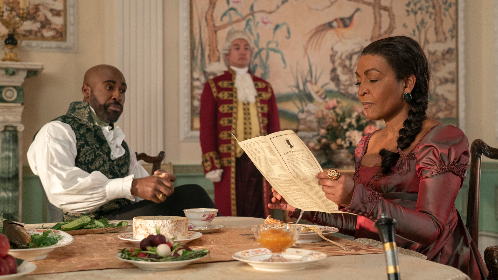 Lady Danbury and Lord Marcus Anderson sit at a table while Lady Danbury reads the latest Lady Whistledown