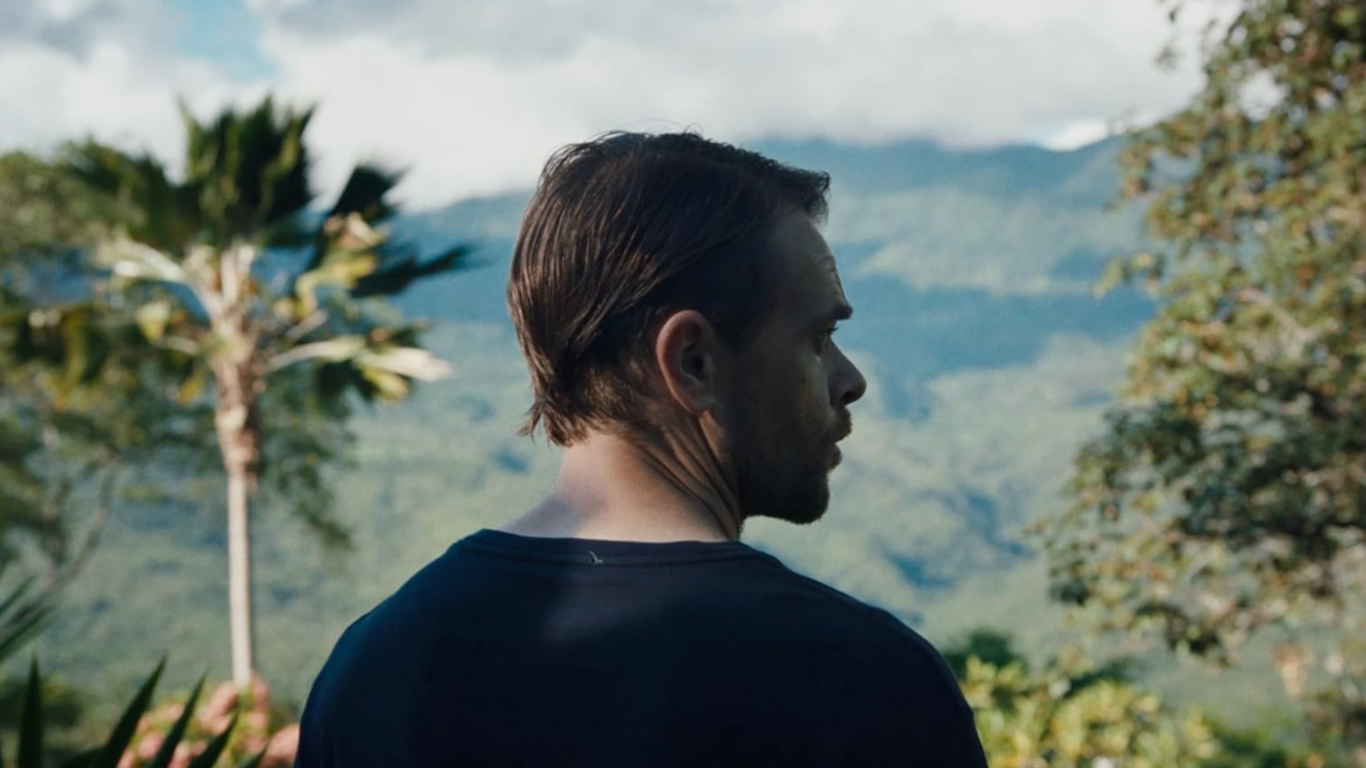 A man stands with his back to the camera with a view of Latin America