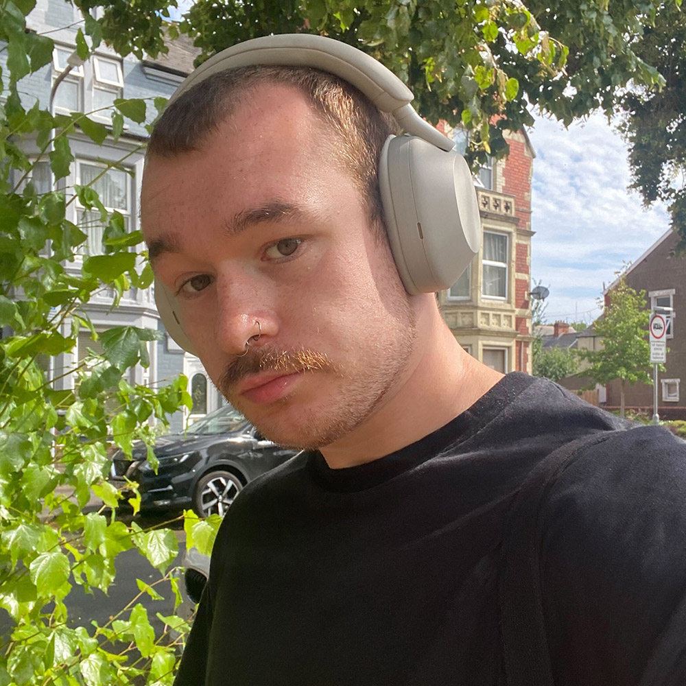 A headshot of a person wearing headphones with a tree in the background