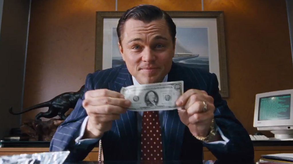 Jordan Belfort holding up a dollar bill in front of the camera in The Wolf of Wall Street.