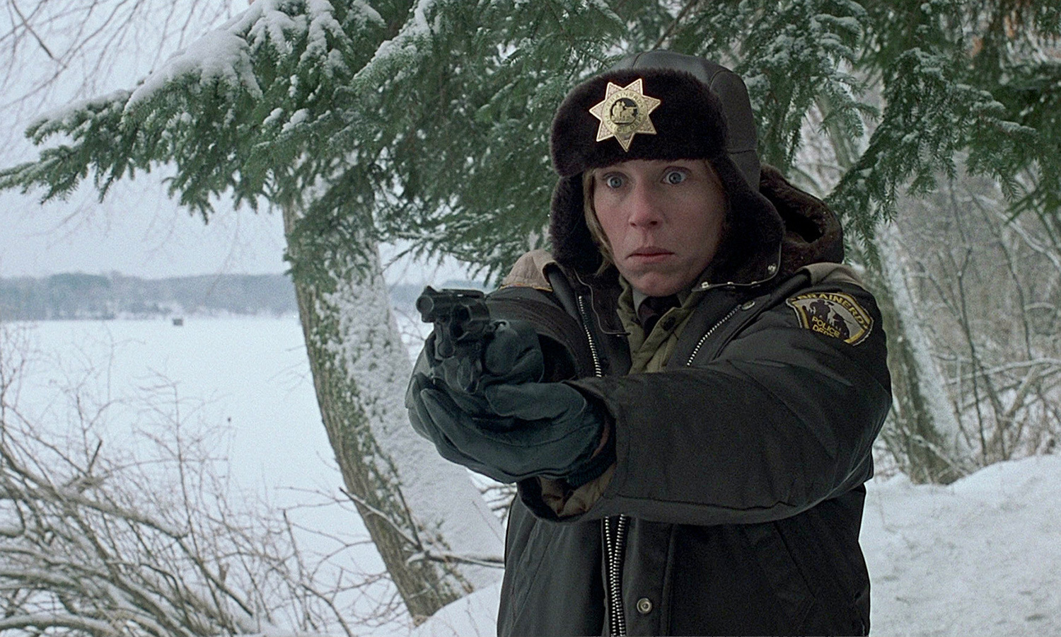 Frances McDormand holds up a gun outside in the snow while wearing a police uniform