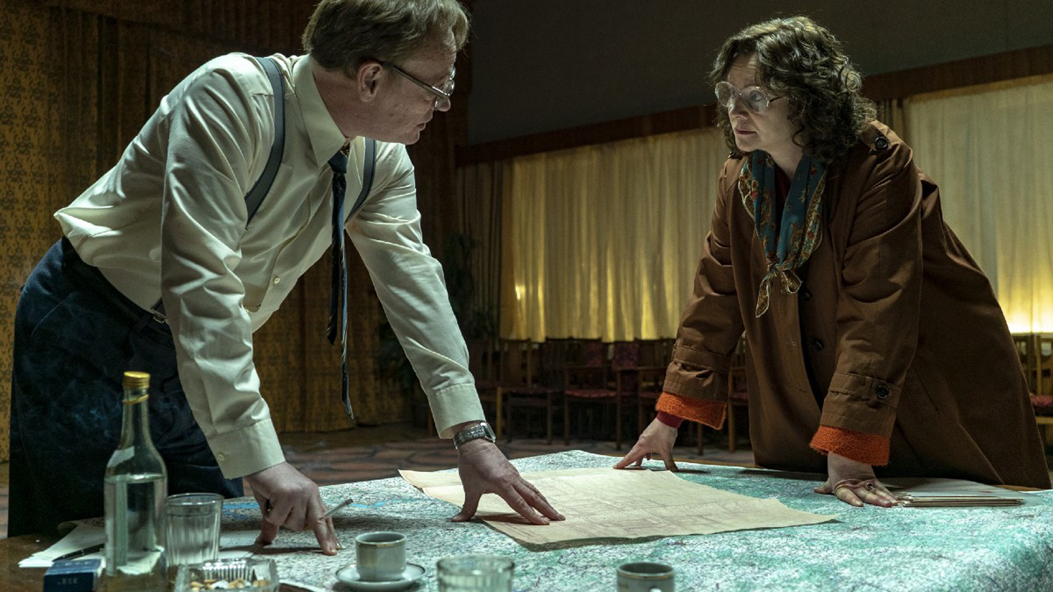 Two characters look at one another with maps on a table in Chernobyl