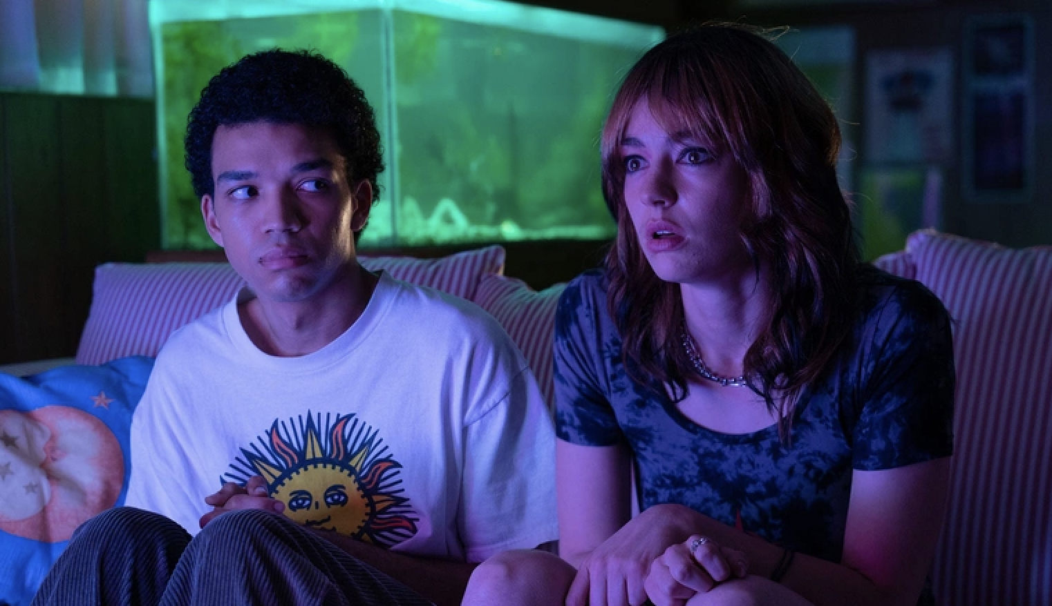 Justice Smith and Brigette Lundy-Paine sitting in front of a TV