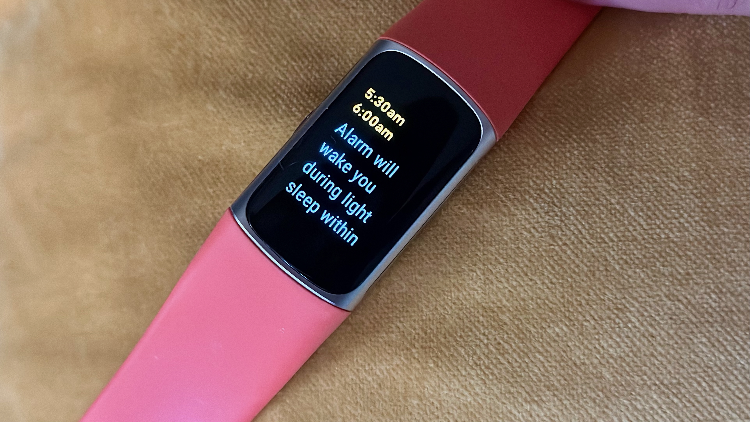 The Fitbit Charge 6 sitting on a pillow, showing an alarm window of 5:30-6:00am, then the words 