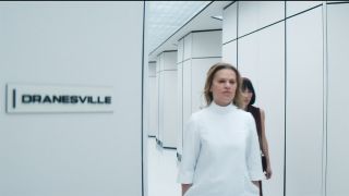 Gemma's nurse and Gemma walking down a corridor with a door bearing the sign Dranesville on it in Severance season 2