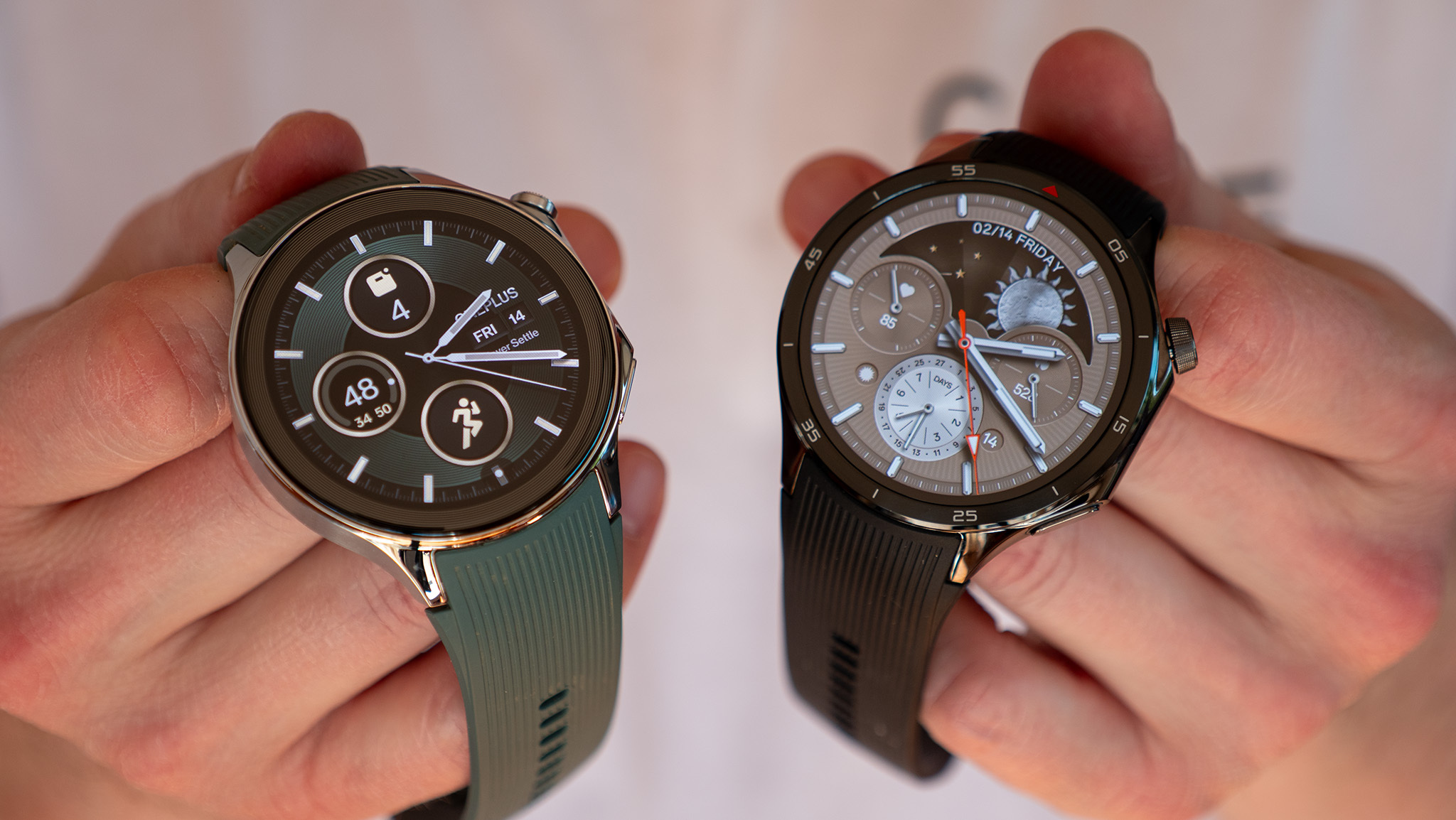 The OnePlus Watch 2 (left) and OnePlus Watch 3 (right) held in two hands, showing their default watch faces.