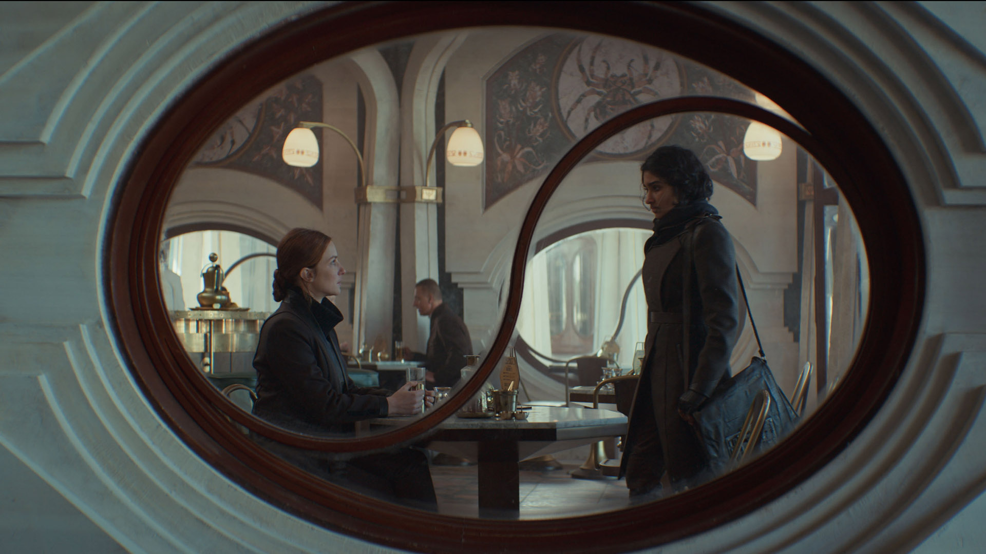 Vel sitting in a cafe as Cinta standing by her table in Andor season 2