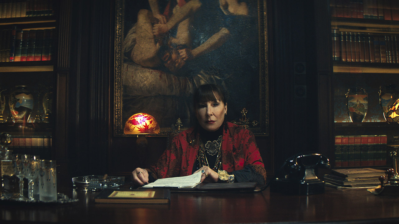 Angelica Huston's The Director sitting at a table signing a document in From the World of John Wick: Ballerina