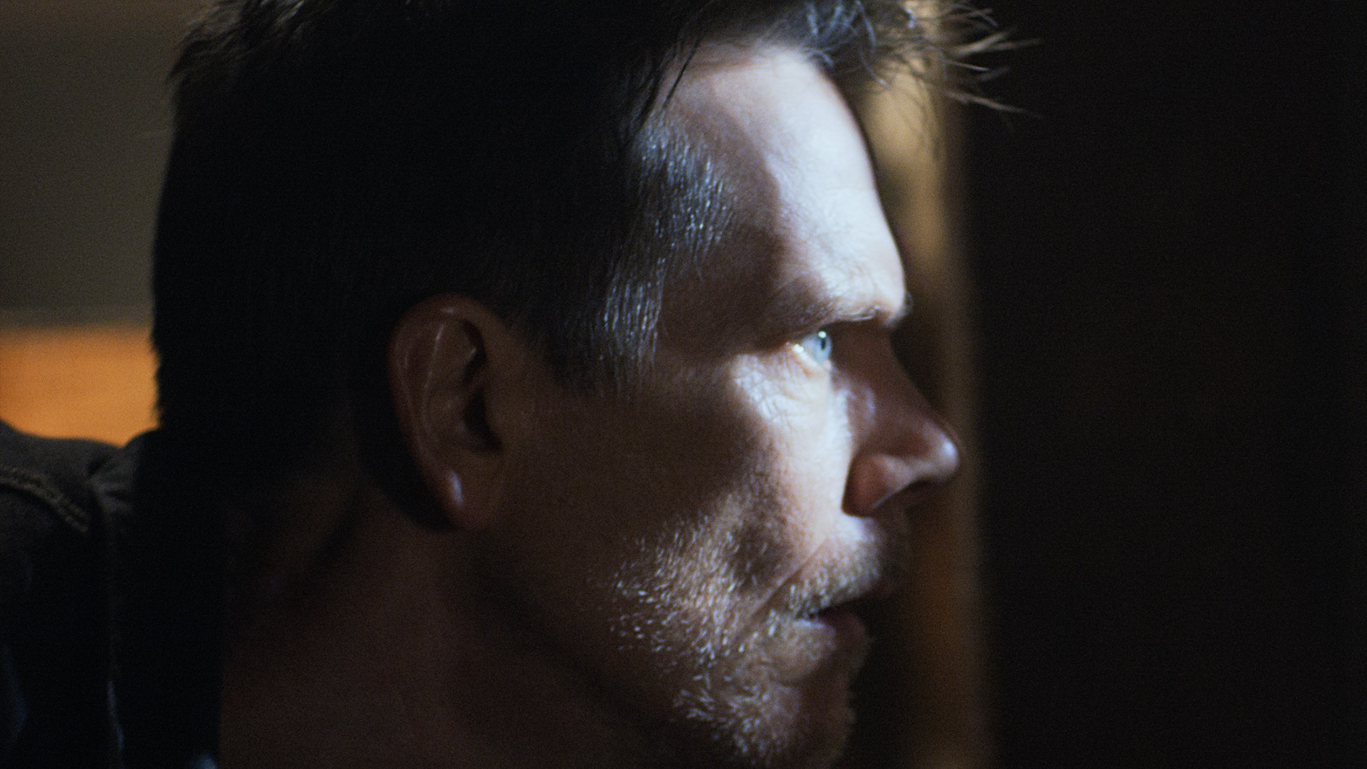 The side of Kevin Bacon's face is shown peering through a gap